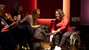 Eine junge Frau im Rollstuhl spielt im Kino mit einem Blindenführhund