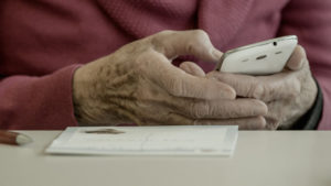 Die Hände einer alten Frau halten ein Smartphone.