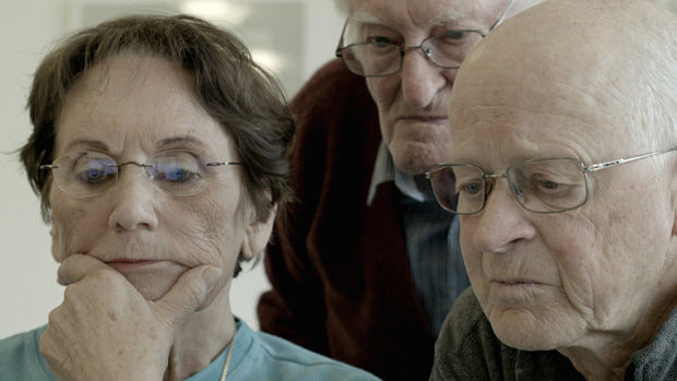 Three elderly persons looking helplessly at a computer screen