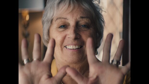 Eine ältere Frau mit kurzem blnden Haar streckt lächelnd ihre zehn Finger in Richtung Kamera