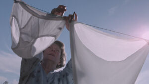 Eine alte Frau im Bademantel hängt im Garten Männerunterwäsche auf